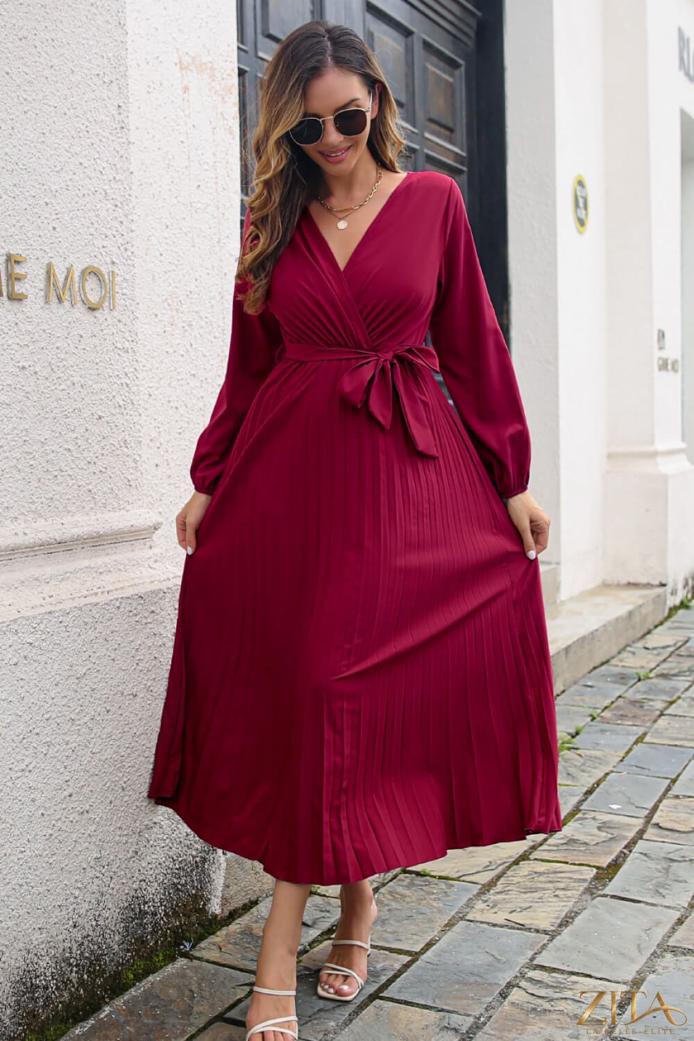 Zita La Belle Elite pleated long sleeve surplice maxi dress with flowing fabric and elegant design, shown on a model.
