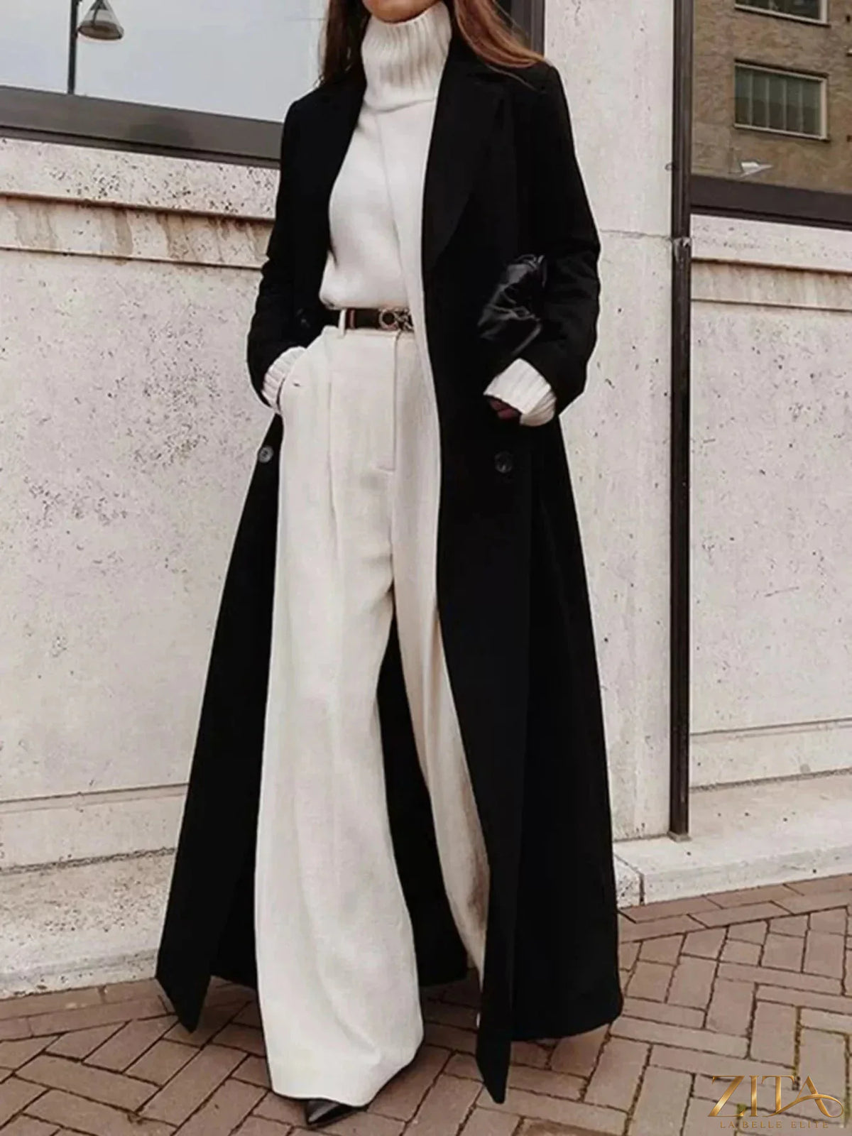 Zita La Belle Elite double-breasted longline overcoat hanging on a wooden hanger, showcasing tailored black outerwear with wide lapels.