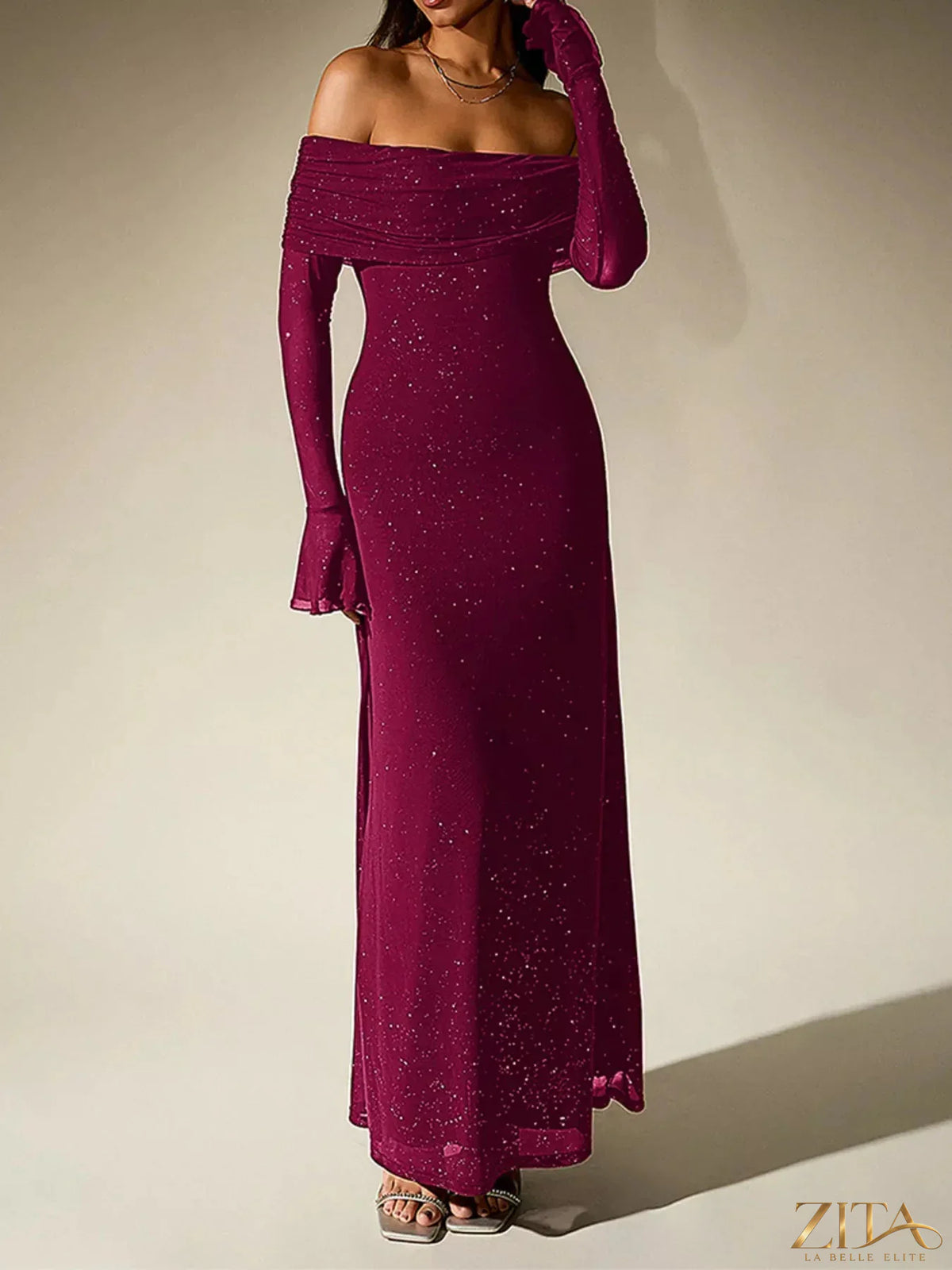 Zita La Belle Elite glitter off-shoulder maxi dress displayed on a hanger with flowing fabric and sparkling details.