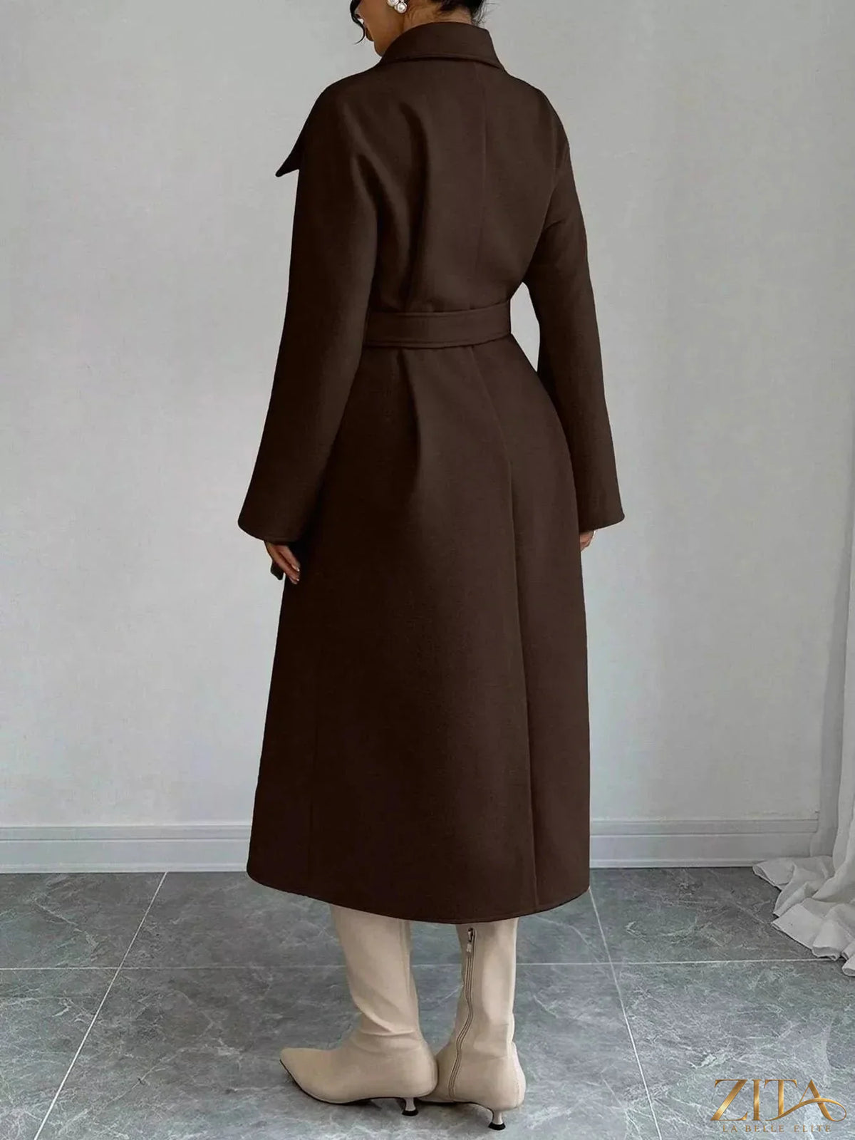 Zita La Belle Elite double-breasted longline coat hanging on a wooden hanger, showcasing its tailored design and neutral color.