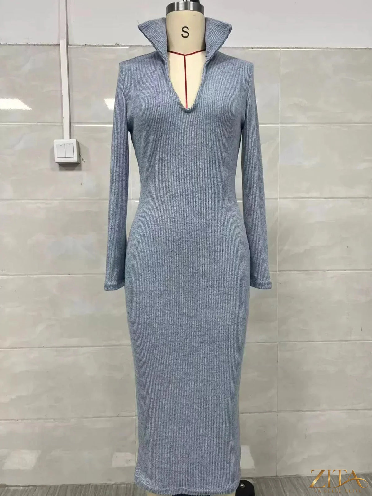Zita La Belle Elite ribbed knit V-neck sweater dress hanging on a wooden hanger, showcasing its fitted ribbed texture and deep V neckline.