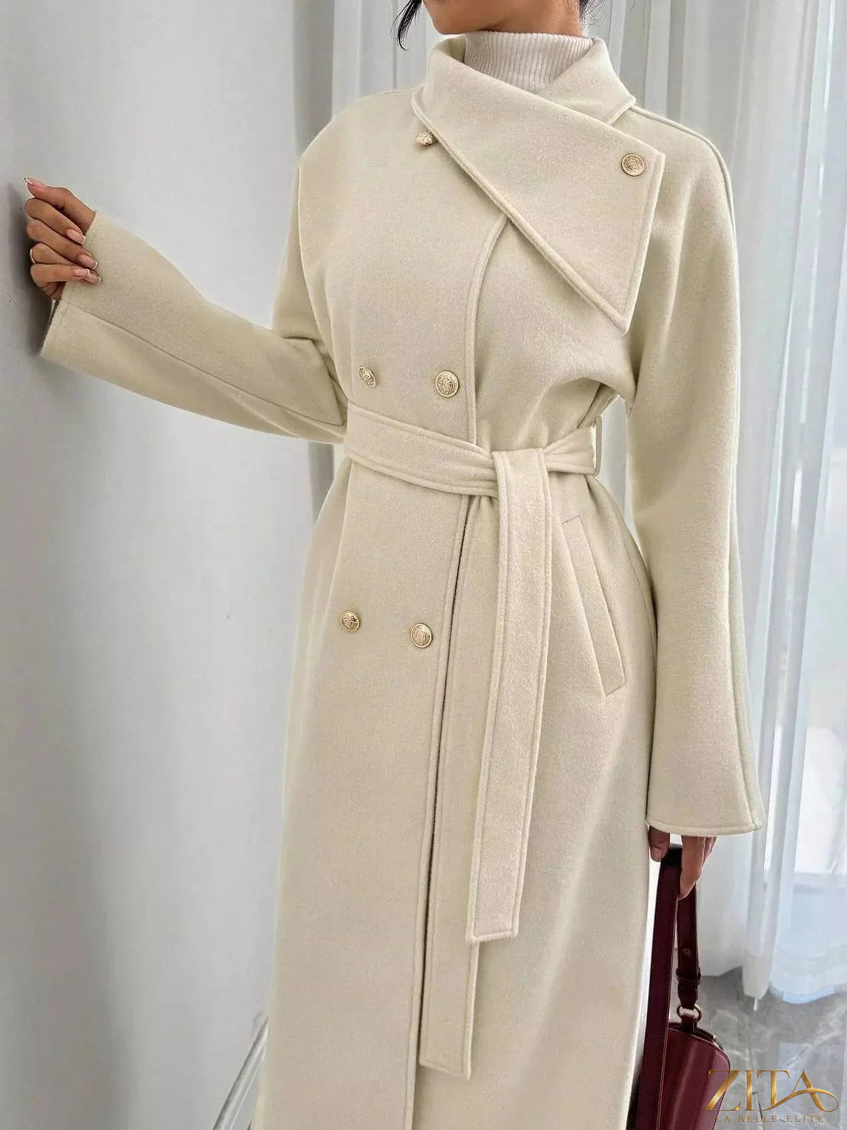 Zita La Belle Elite double-breasted longline coat in neutral fabric, shown hanging on a wooden hanger.