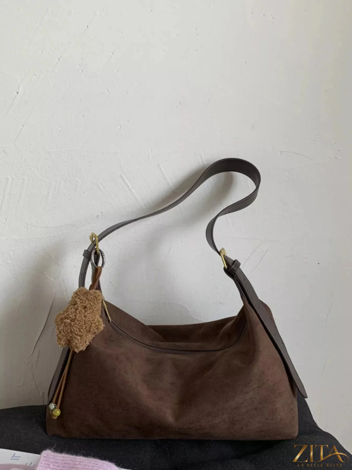 Zita La Belle Elite solid color suede hobo crossbody bag with rounded shape and adjustable strap on a neutral background.