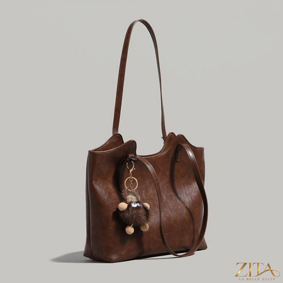 Zita La Belle Elite leather tote bag featuring a decorative charm, shown in brown with sturdy handles and spacious interior.